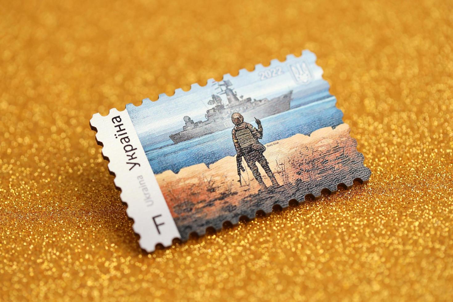 TERNOPIL, UKRAINE - SEPTEMBER 2, 2022 Famous Ukrainian postmark with russian warship and ukrainian soldier as wooden souvenir on golden glitter background photo