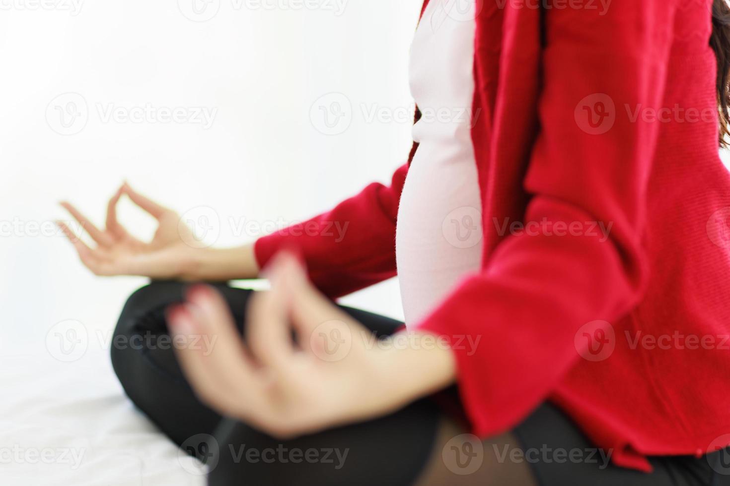 Pregnant woman sits in bed in her bedroom meditating alone in peace and happiness. The new mother resting by sitting down to chill out. photo