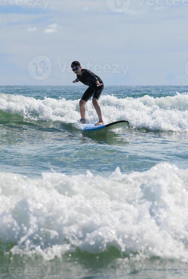 Young boy wearing swimming goggles stable stands on soft board while practicing surfing in beginner's class. photo