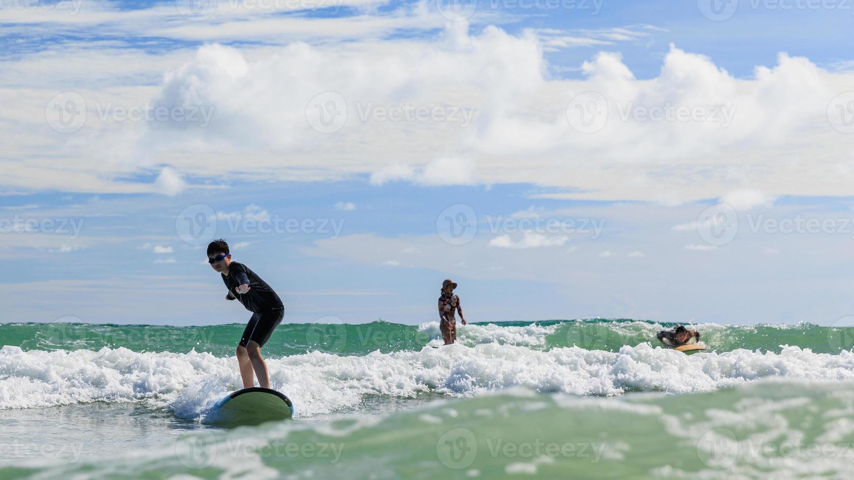 Young boy wearing swimming goggles stands on soft board while practicing surfing in beginner's class. photo