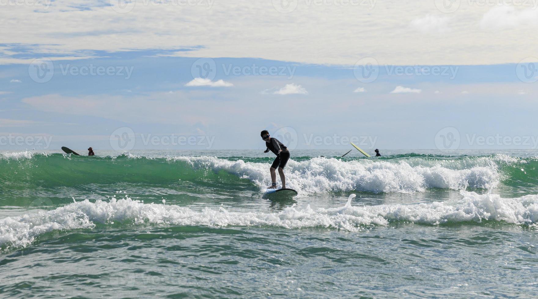 Young boy wearing swimming goggles stable stands on soft board while practicing surfing in beginner's class. photo