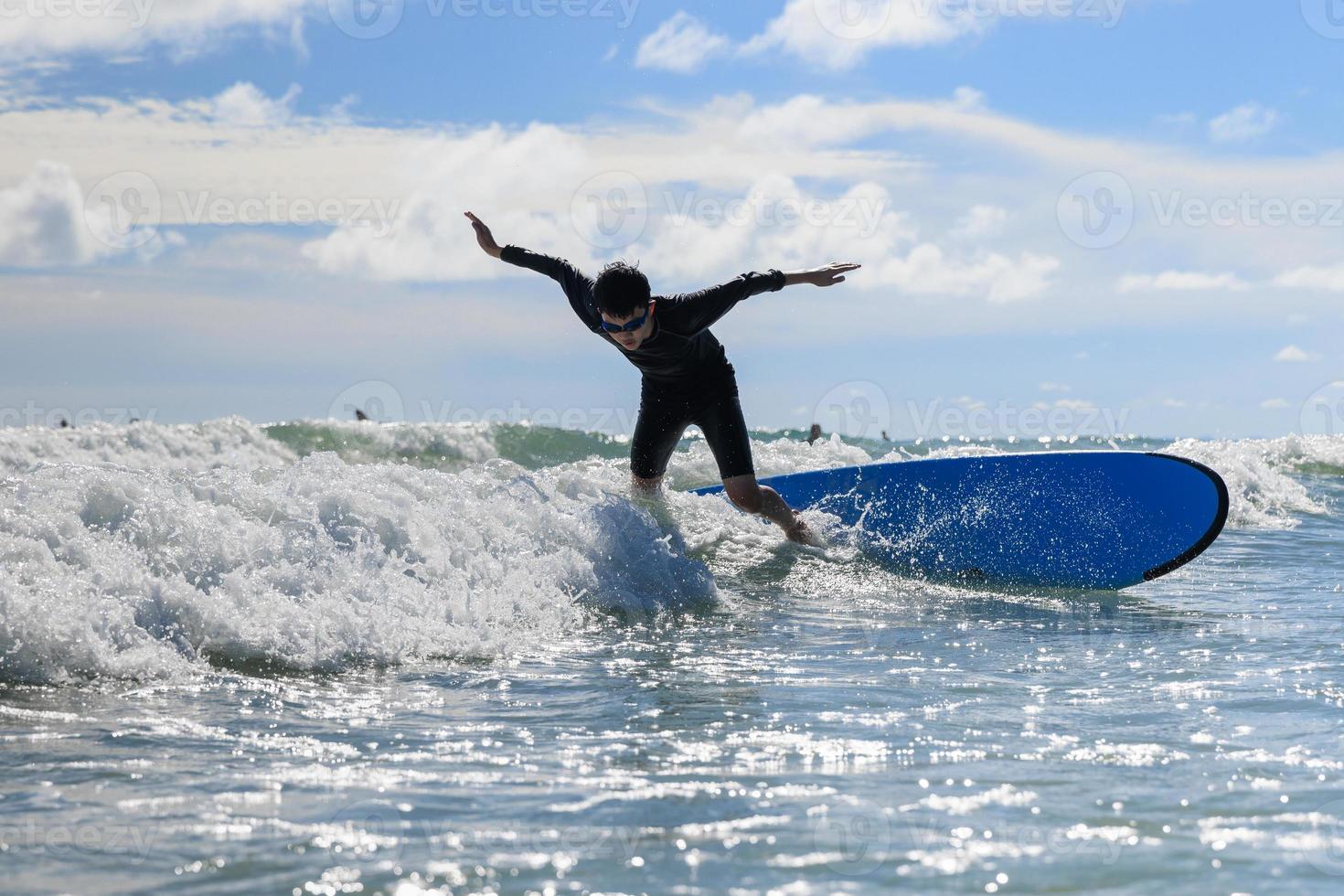 Young boy, new student in surfing, loses his body balance and falls from surfboard into the water during class. photo