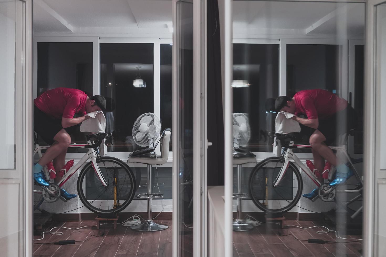 hombre en bicicleta en el entrenador de la máquina que está haciendo ejercicio en el hogar por la noche jugando al juego de carreras de bicicletas en línea foto