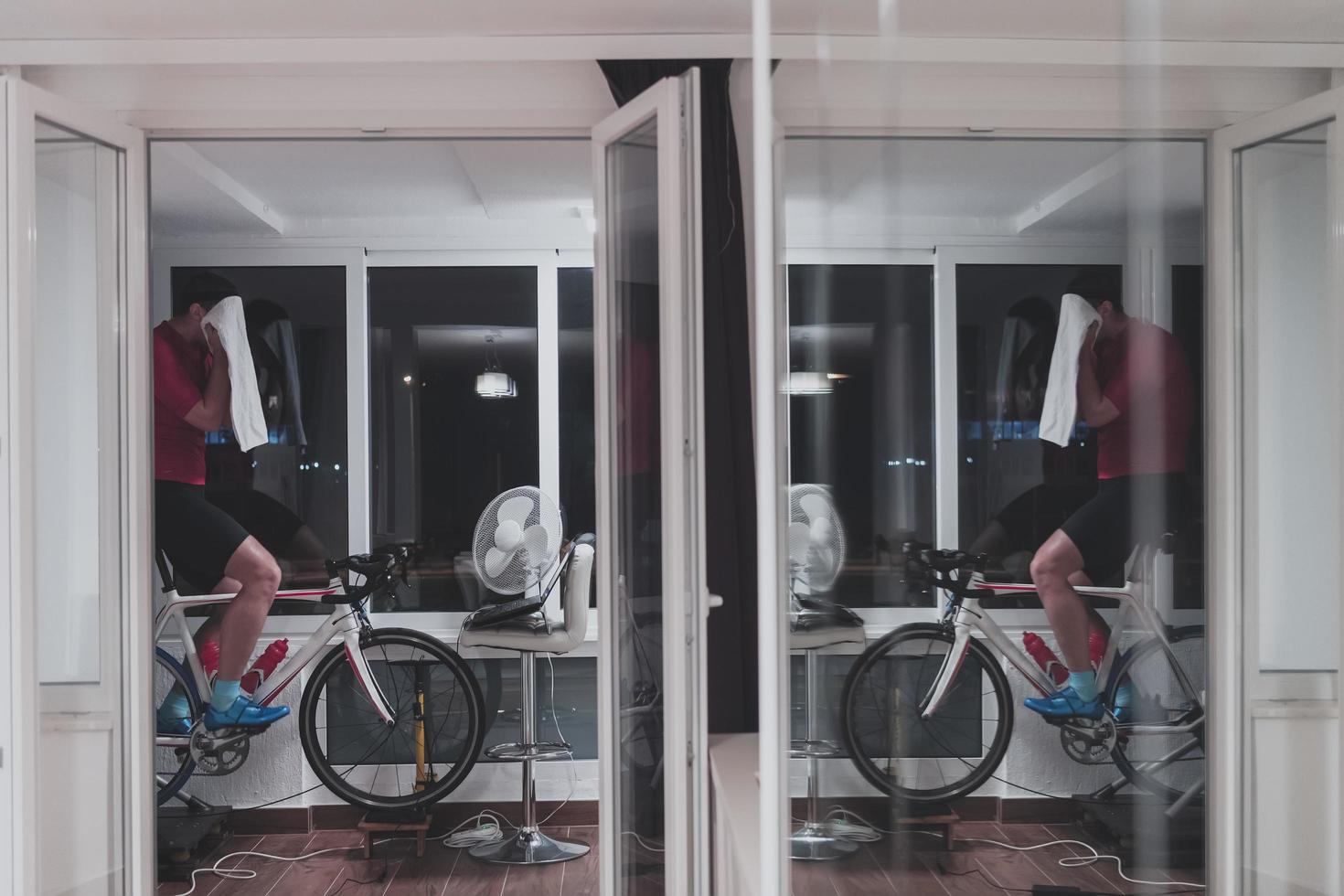 hombre en bicicleta en el entrenador de la máquina que está haciendo ejercicio en el hogar por la noche jugando al juego de carreras de bicicletas en línea foto