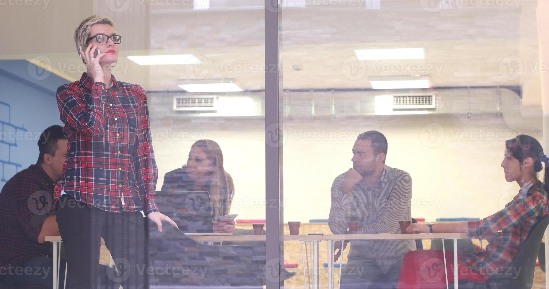 Business Woman Looking Through A Window And using On A Cell Phone during bussines meeting photo