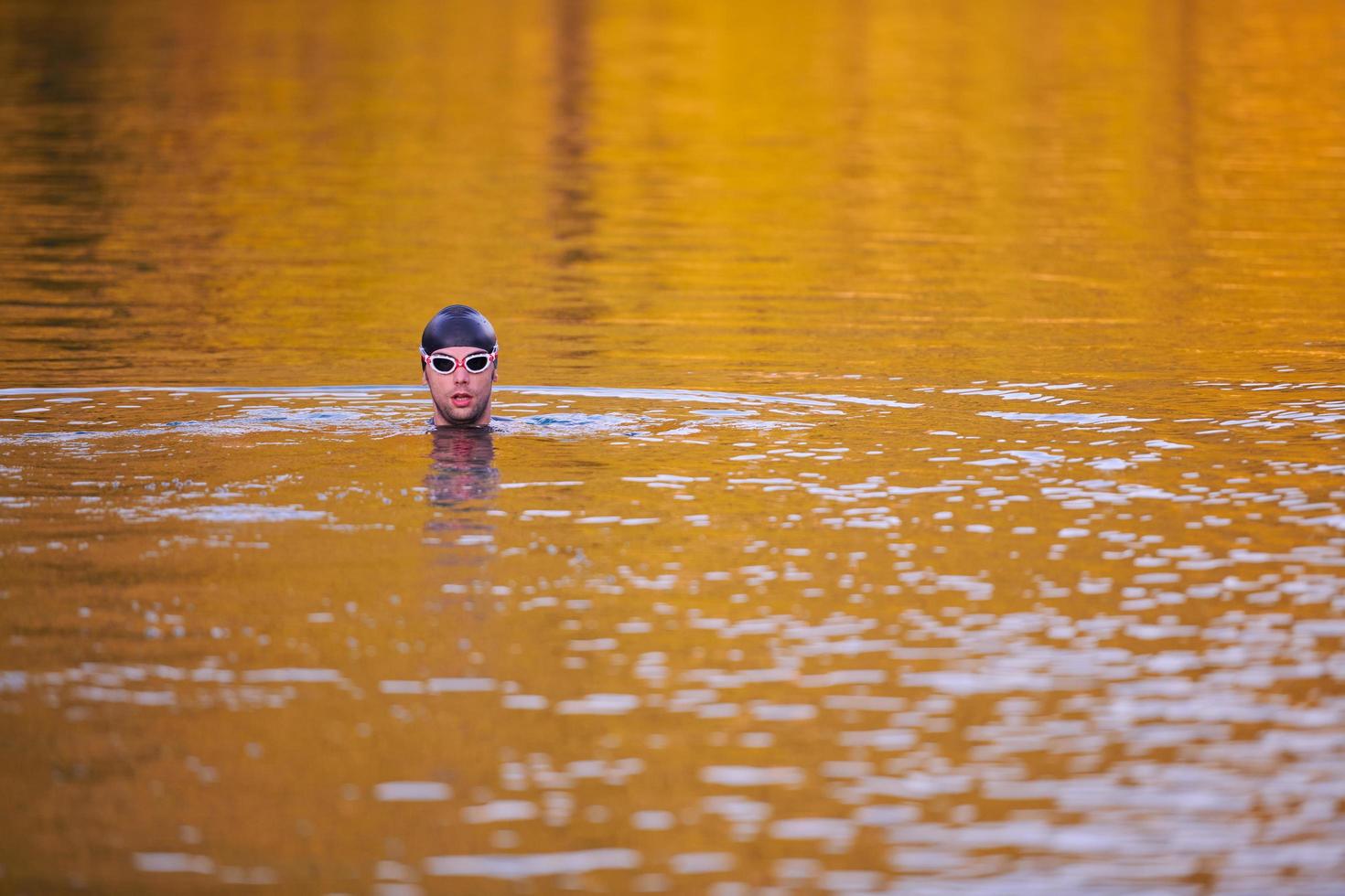 triathlon athlete swimming on lake in sunrise  wearing wetsuit photo
