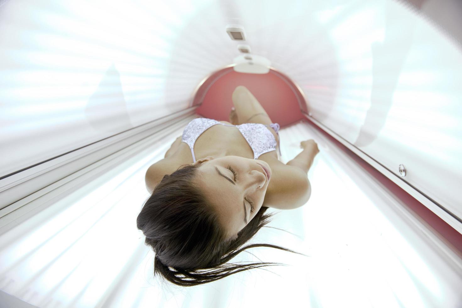 Beautiful young woman tanning in solarium photo