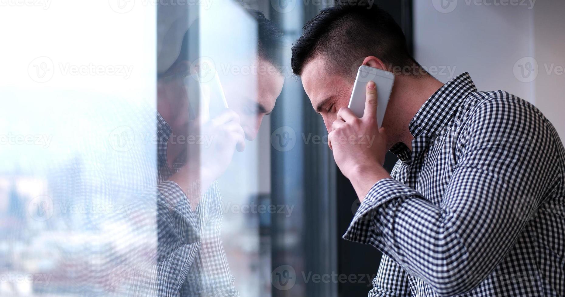 hombre de negocios hablando por teléfono celular, mirando por la ventana de la oficina foto