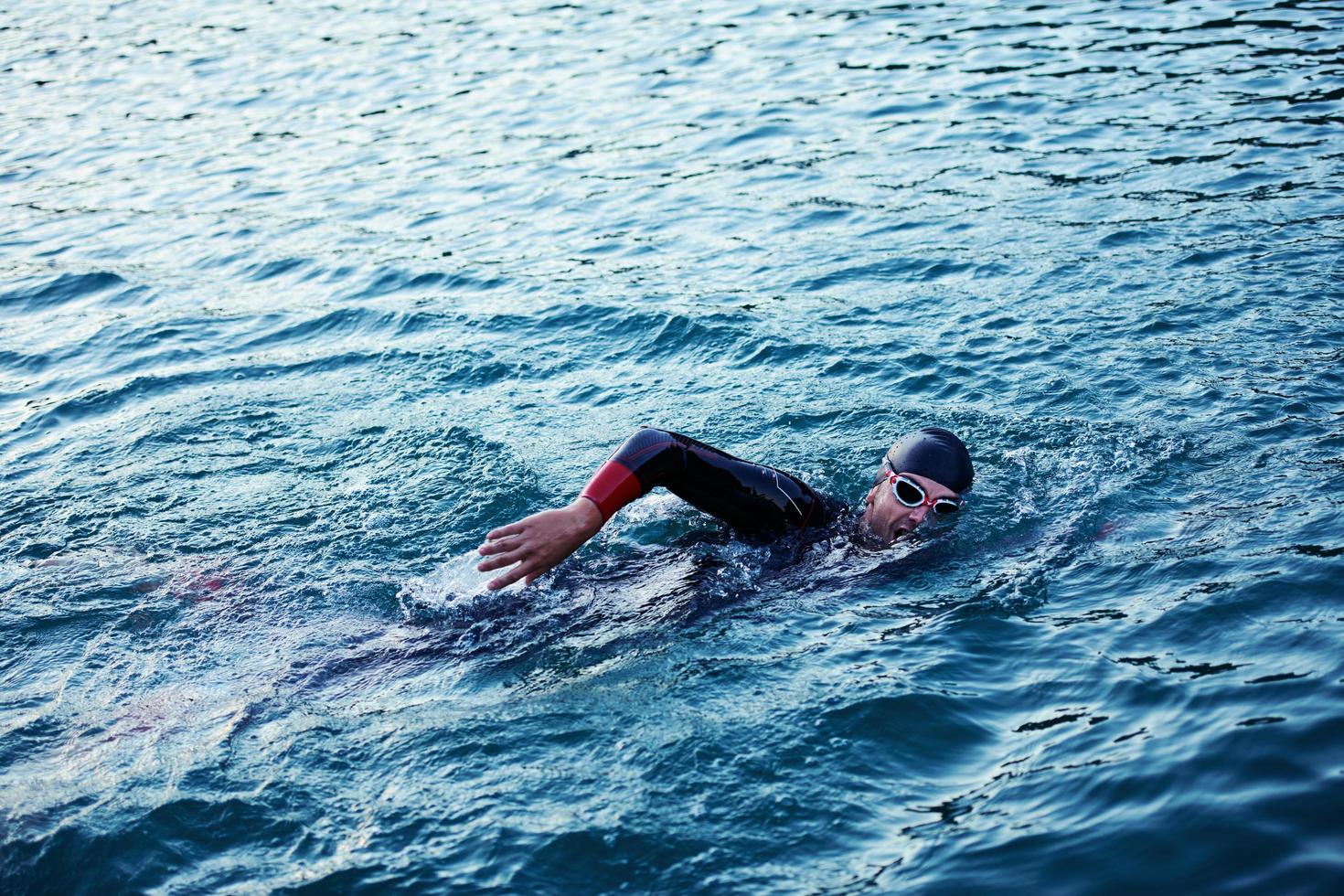 triathlon athlete swimming on lake in sunrise  wearing wetsuit photo