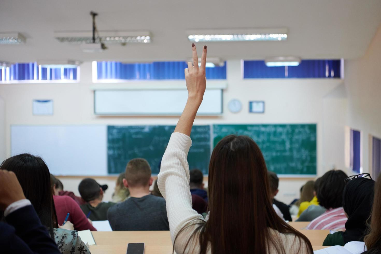 female student sitting in the class and raising hand up photo