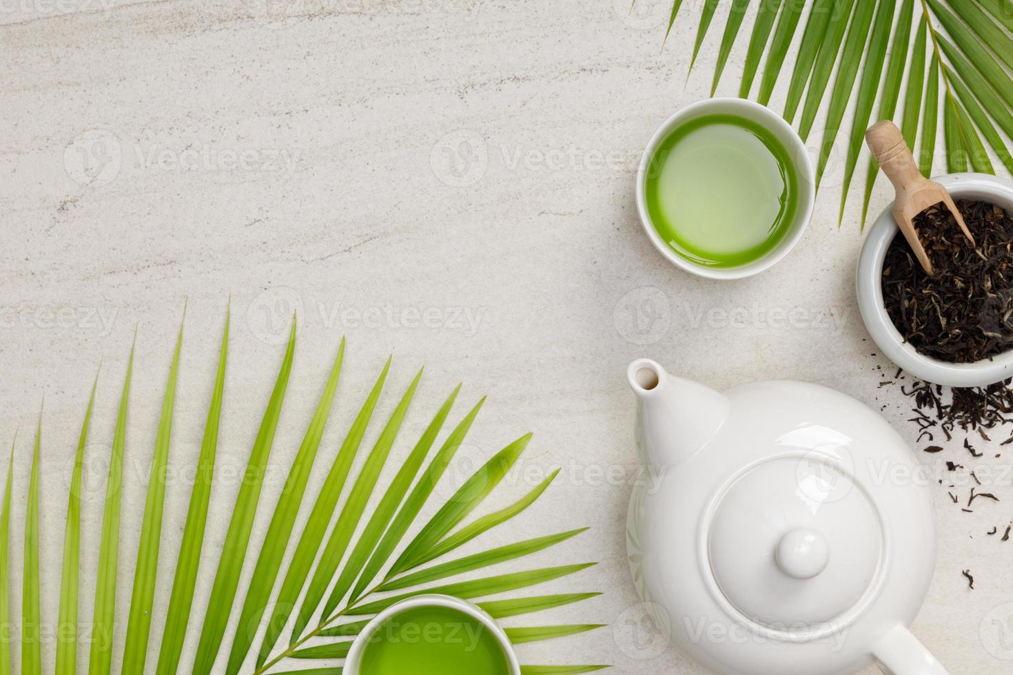 Glass teapot and thermo cup with green tea and dried apricots on wooden  table against defocused sofa with pillows. Front view. Mock-up Stock Photo