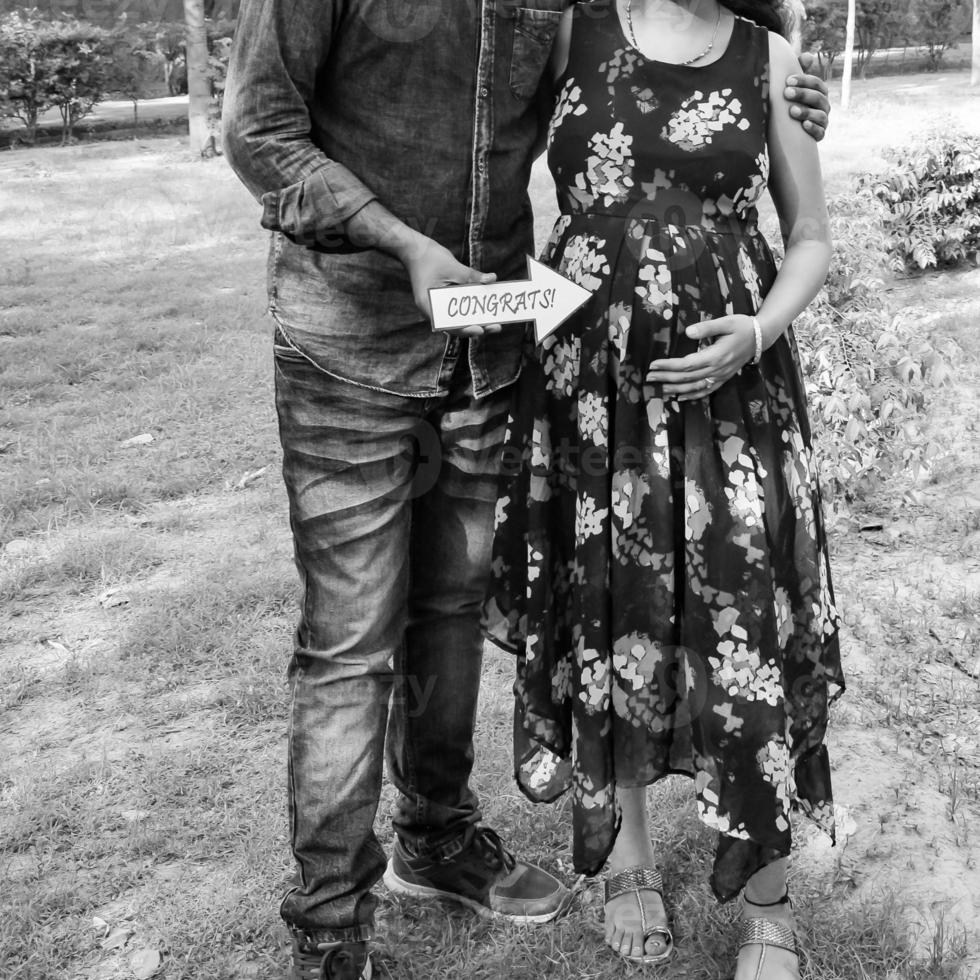 Indian couple posing for maternity baby shoot. The couple is posing in a lawn with green grass and the woman is falunting her baby bump in Lodhi Garden in New Delhi, India - Black and White photo