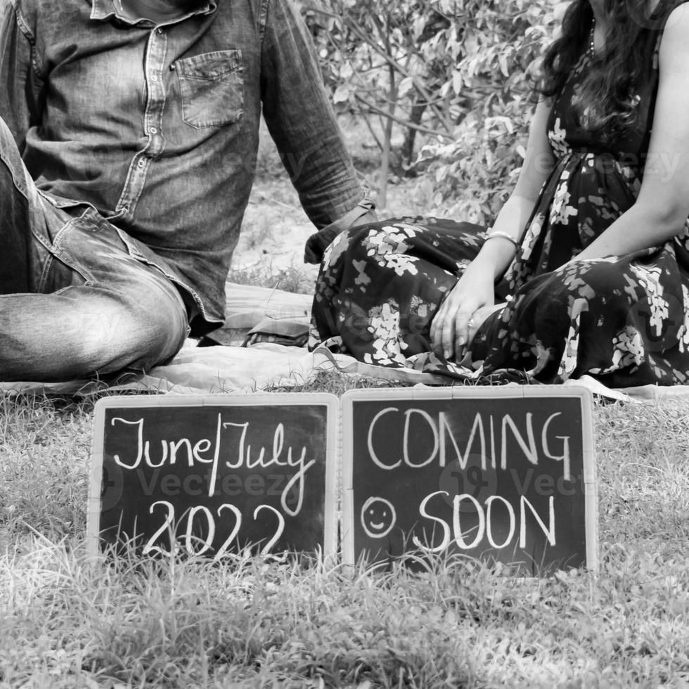 Indian couple posing for maternity baby shoot. The couple is posing in a lawn with green grass and the woman is falunting her baby bump in Lodhi Garden in New Delhi, India - Black and White photo