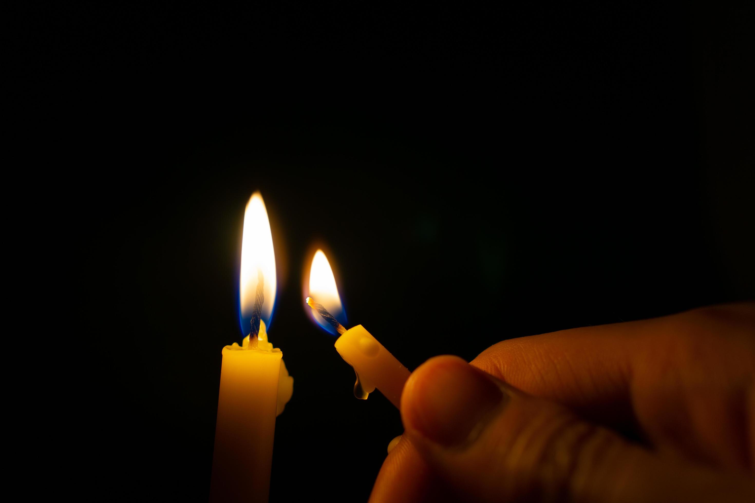 Hand holding burning yellow candle to light candle in the dark 11637558