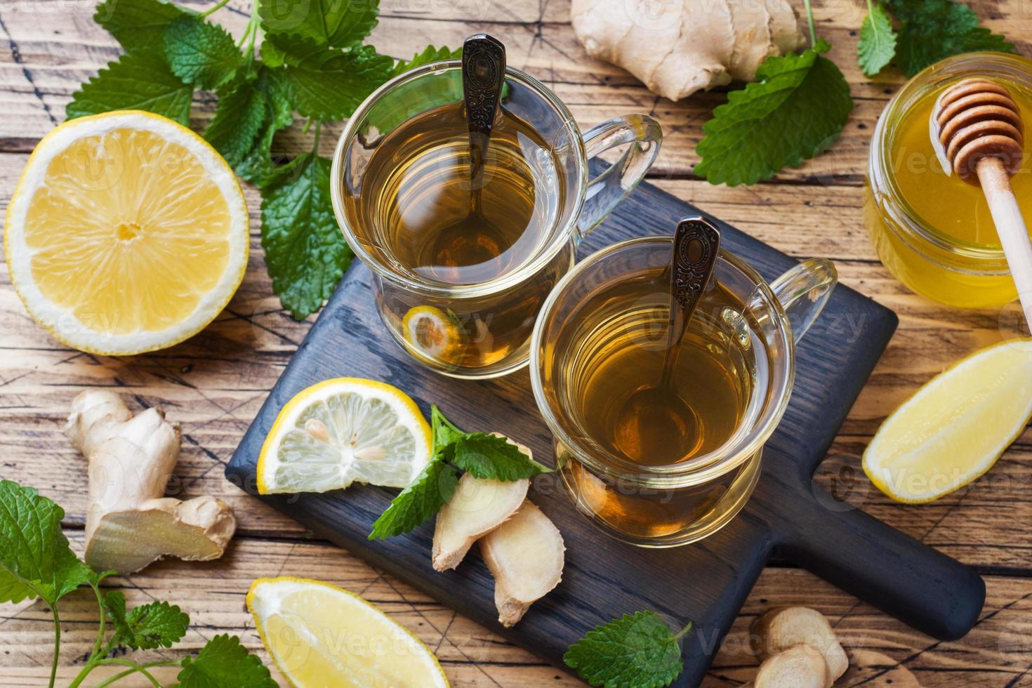 dos tazas de té de hierbas naturales jengibre limón menta y miel sobre un fondo de madera. foto