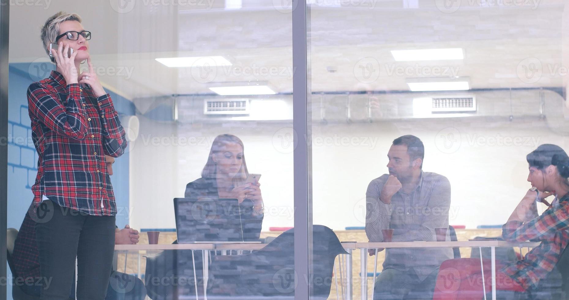 Business Woman Looking Through A Window And using On A Cell Phone during bussines meeting photo