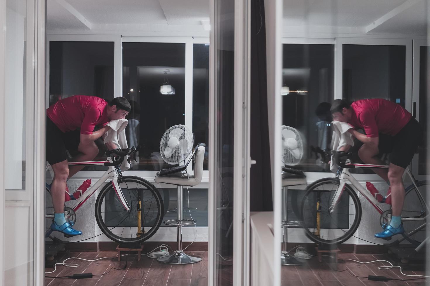 hombre en bicicleta en el entrenador de la máquina que está haciendo ejercicio en el hogar por la noche jugando al juego de carreras de bicicletas en línea foto