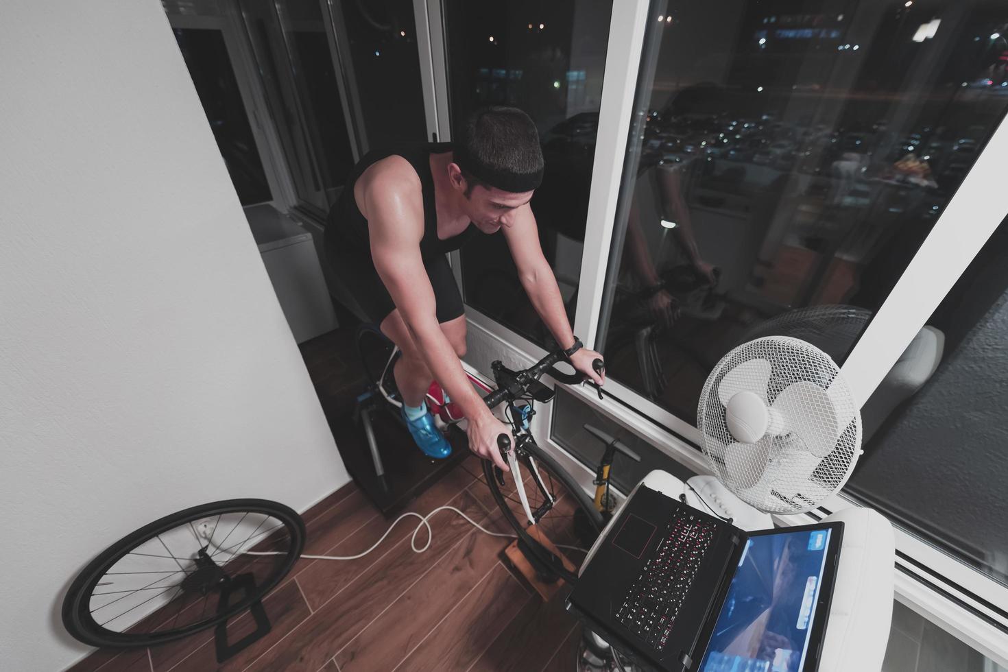 Man cycling on the machine trainer he is exercising in the home at night playing online bike racing game photo