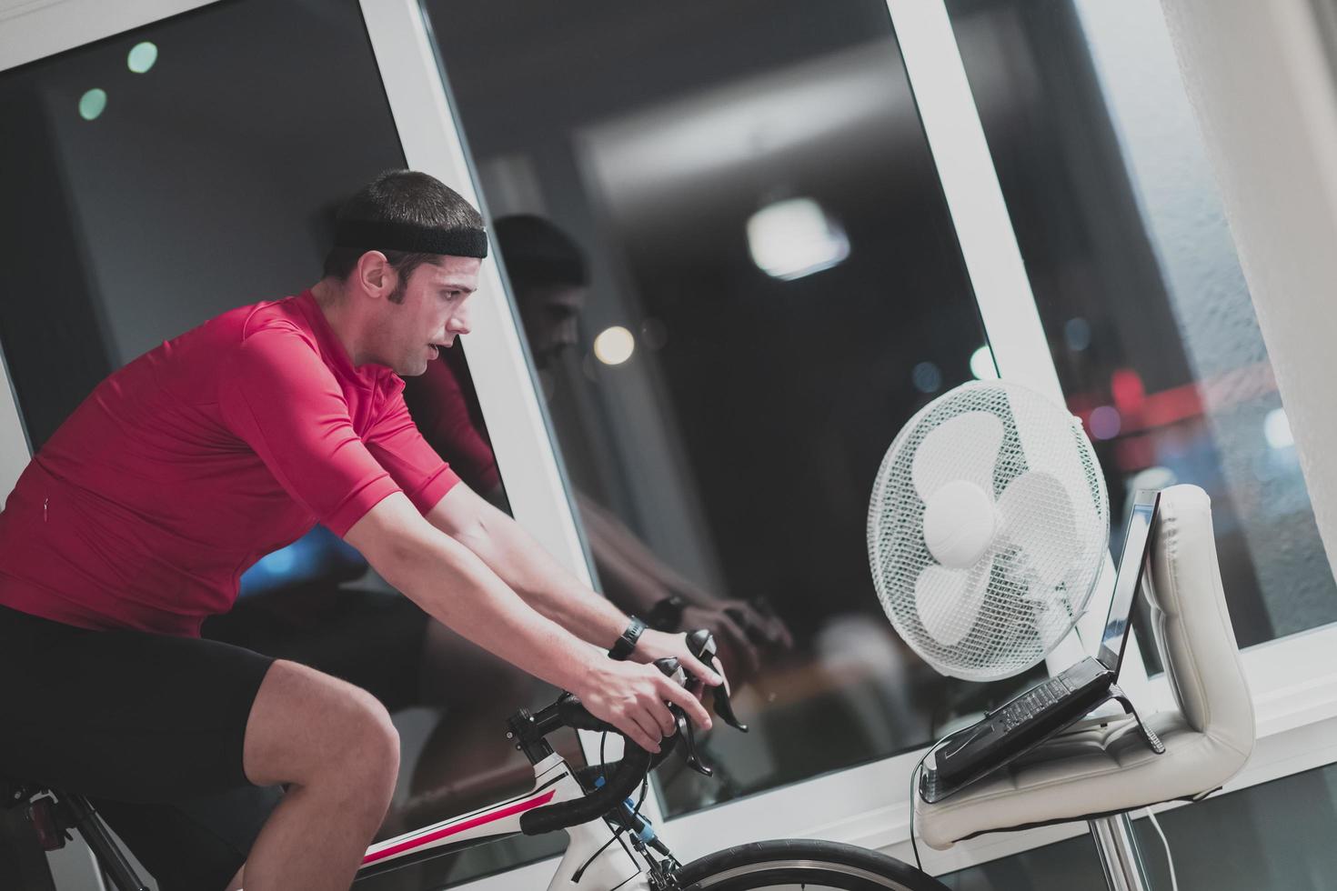 Man cycling on the machine trainer he is exercising in the home at night playing online bike racing game photo