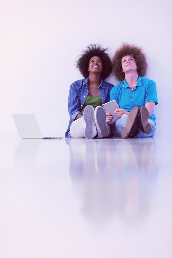 multiethnic couple sitting on the floor with a laptop and tablet photo