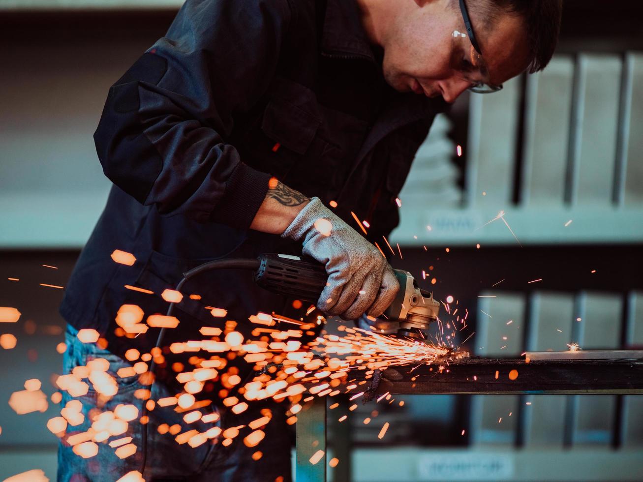 interior de fábrica de ingeniería de industria pesada con trabajador industrial usando amoladora angular y cortando un tubo de metal. contratista en estructuras metálicas de fabricación de cascos y uniformes de seguridad. foto