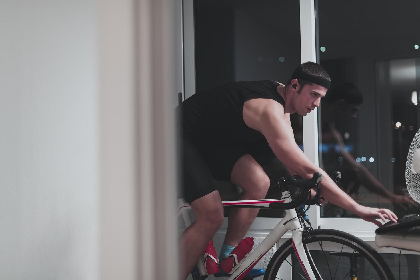 hombre en bicicleta en el entrenador de la máquina que está haciendo ejercicio en el hogar por la noche jugando al juego de carreras de bicicletas en línea foto