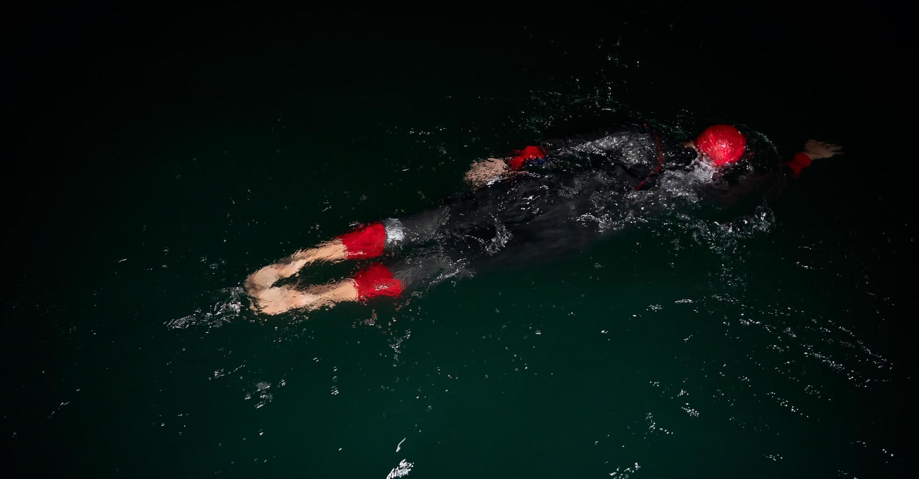 triathlon athlete swimming in dark night  wearing wetsuit photo