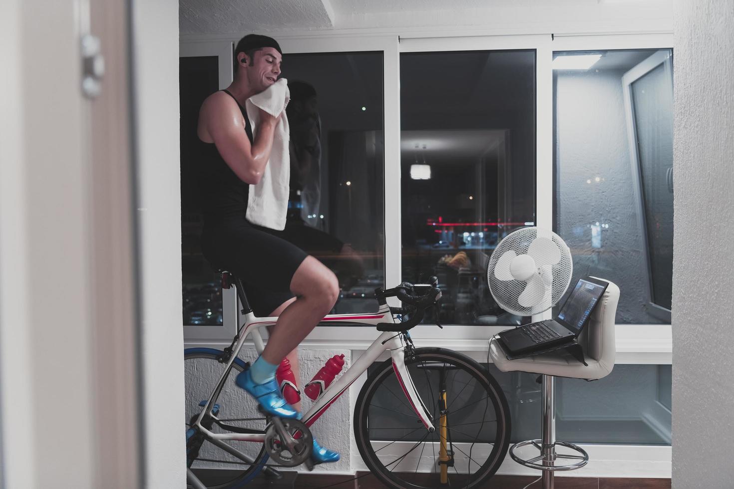 hombre en bicicleta en el entrenador de la máquina que está haciendo ejercicio en el hogar por la noche jugando al juego de carreras de bicicletas en línea foto