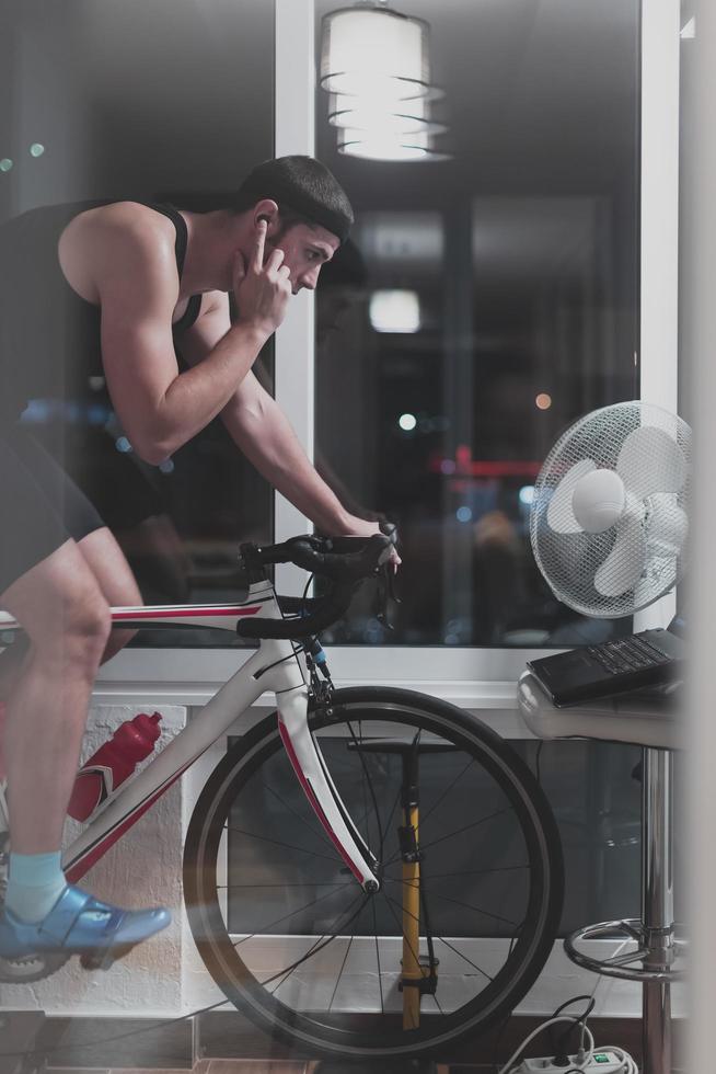 Man cycling on the machine trainer he is exercising in the home at night playing online bike racing game photo