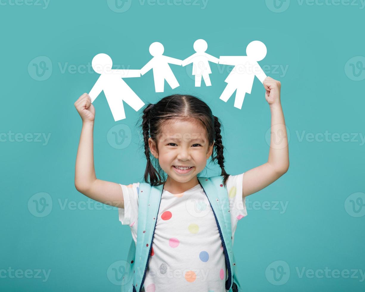 Smiling happy Asian little girl holding paper cut of family, empty space in studio shot isolated on colorful blue background, Happy family concept photo
