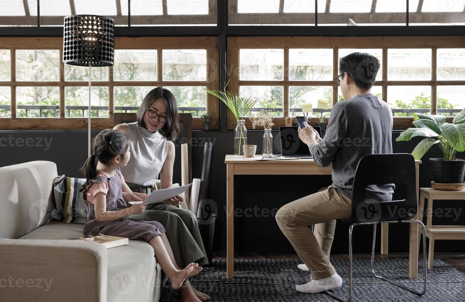 Working from home lifestyle father using smartphone on the desk and child girl learning with her mother on sofa in the living room, Quarantine isolation during the Coronavirus COVID-19 health crisis photo