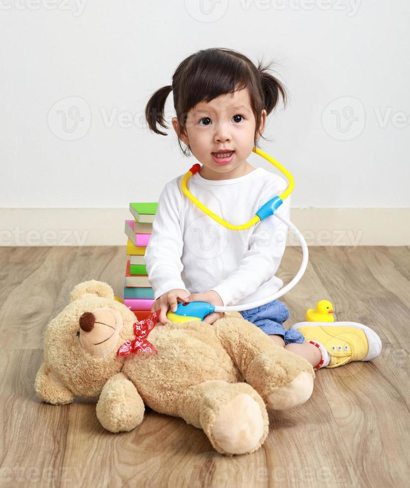 una pequeña doctora asiática juega con un osito de peluche en la habitación. foto