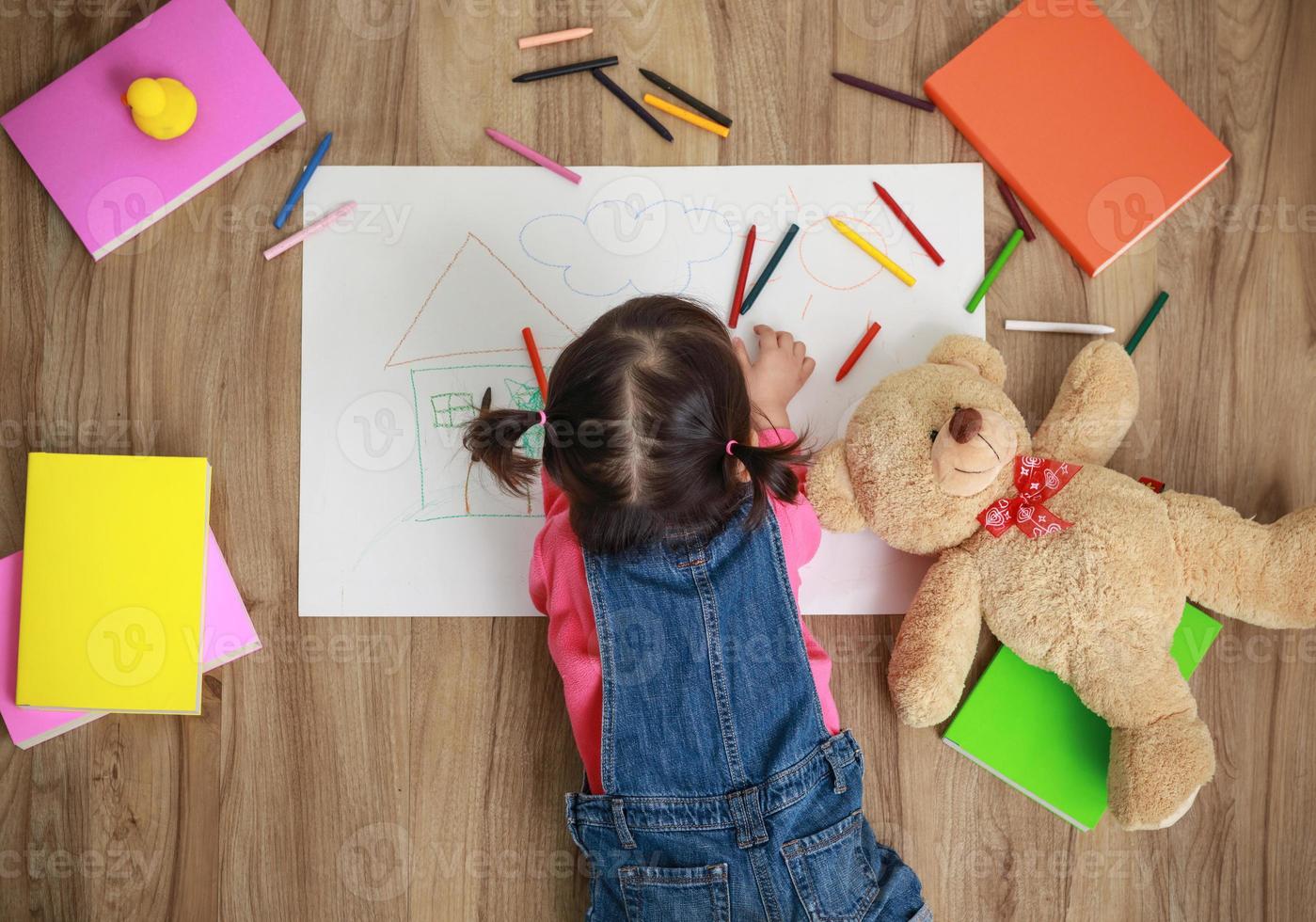 niña asiática dibujando en papel en el suelo interior, vista superior del niño en el suelo foto