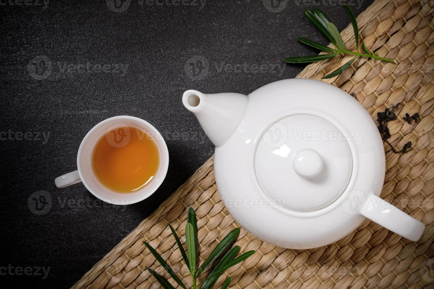 Cup of hot tea with steaming jugs and dry tea on the plate mat on the black stone table background with copyspace for your text. photo