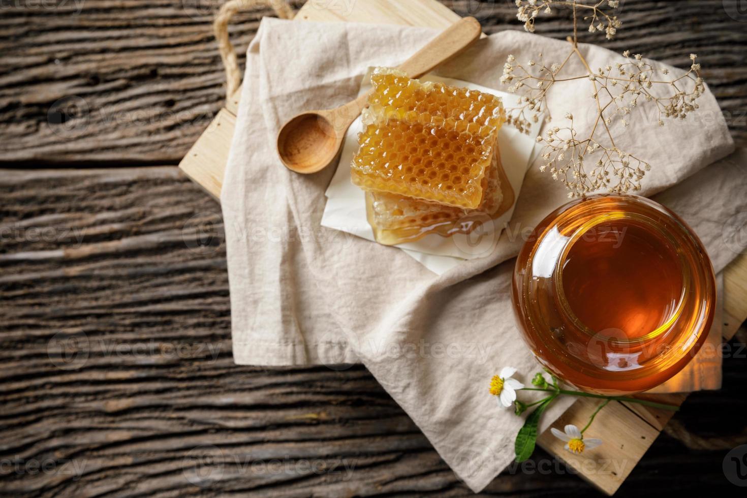 abeja de miel en tarro y panal con cucharón de miel y flor en mesa de madera, productos de abejas por concepto de ingredientes naturales orgánicos foto