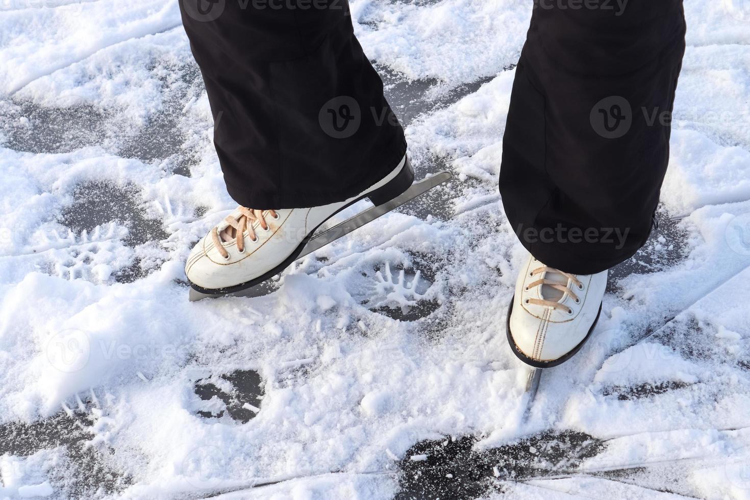 Ciérrese para arriba en los pies de las mujeres que llevan botas de patinaje sobre hielo y que se colocan en el hielo. foto