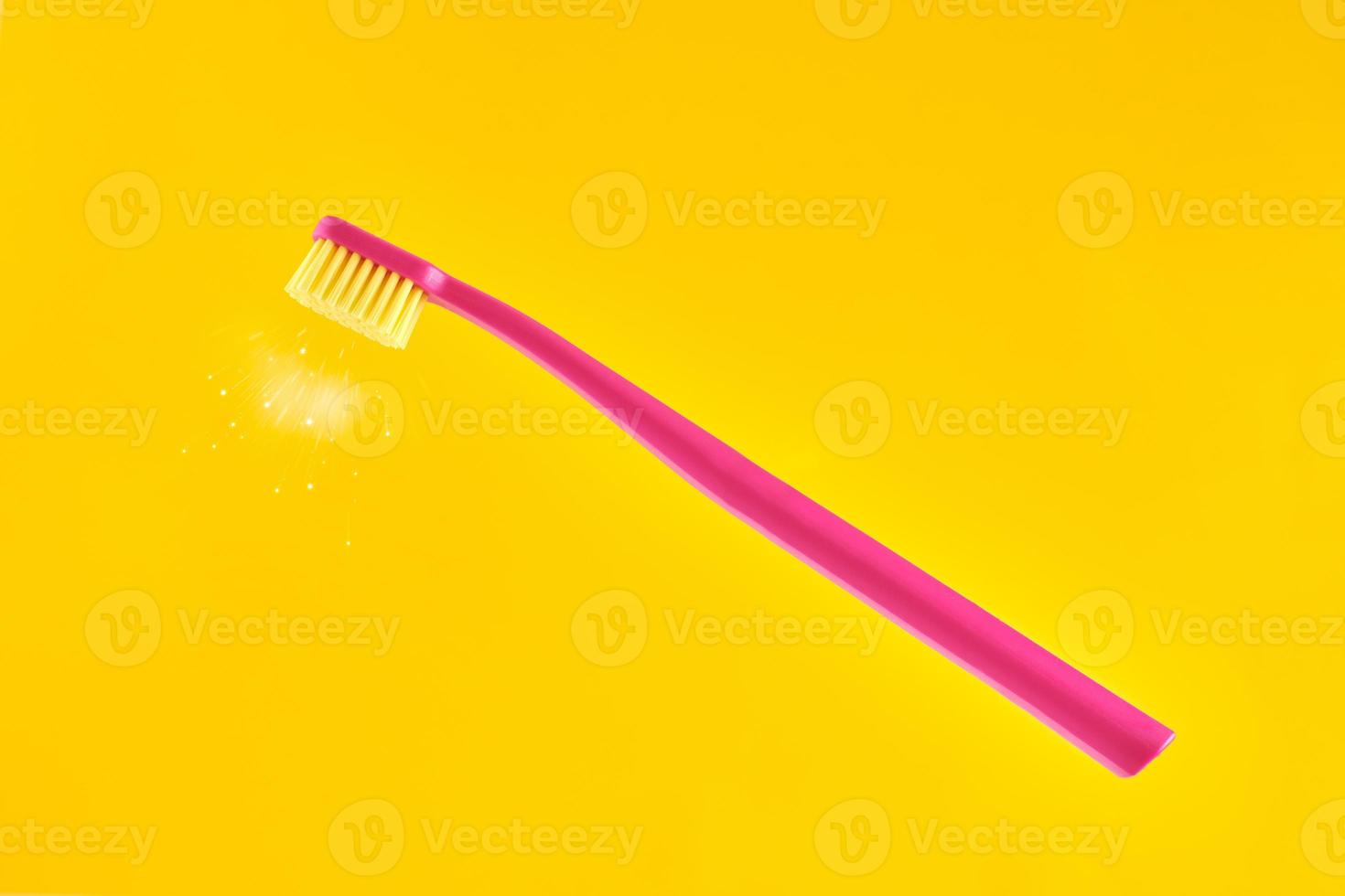 Pink toothbrush on yellow background for oral hygiene to clean teeth, gums and tongue photo