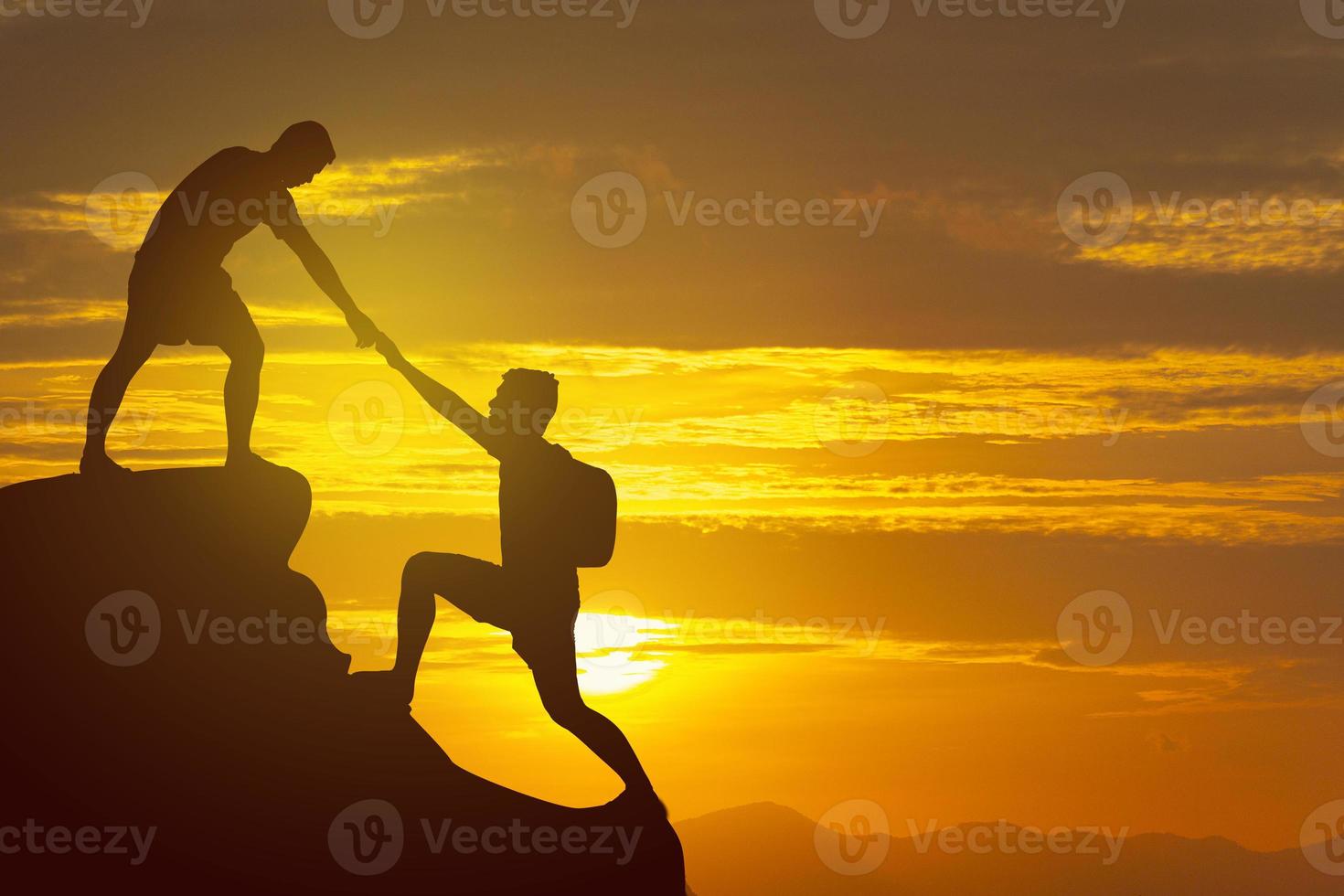 Silhouette Two Male hikers climbing up mountain cliff and one of them giving helping hand. People helping and, team work concept. photo