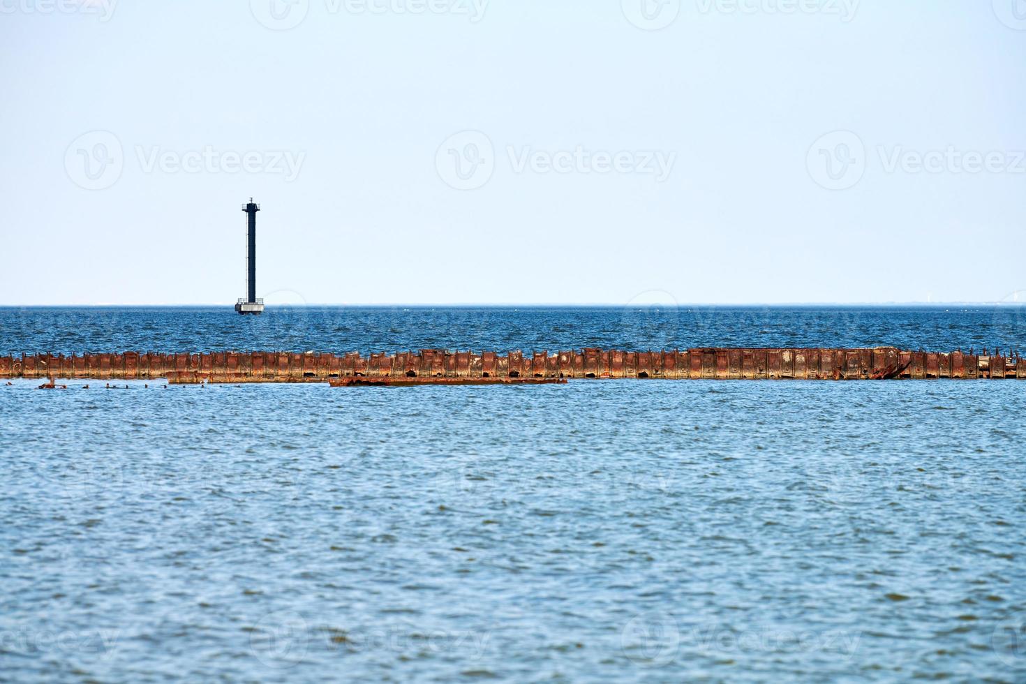 Old abandoned rusty sea pier for mooring boats and yachts on background of calm blue sea, horizon photo