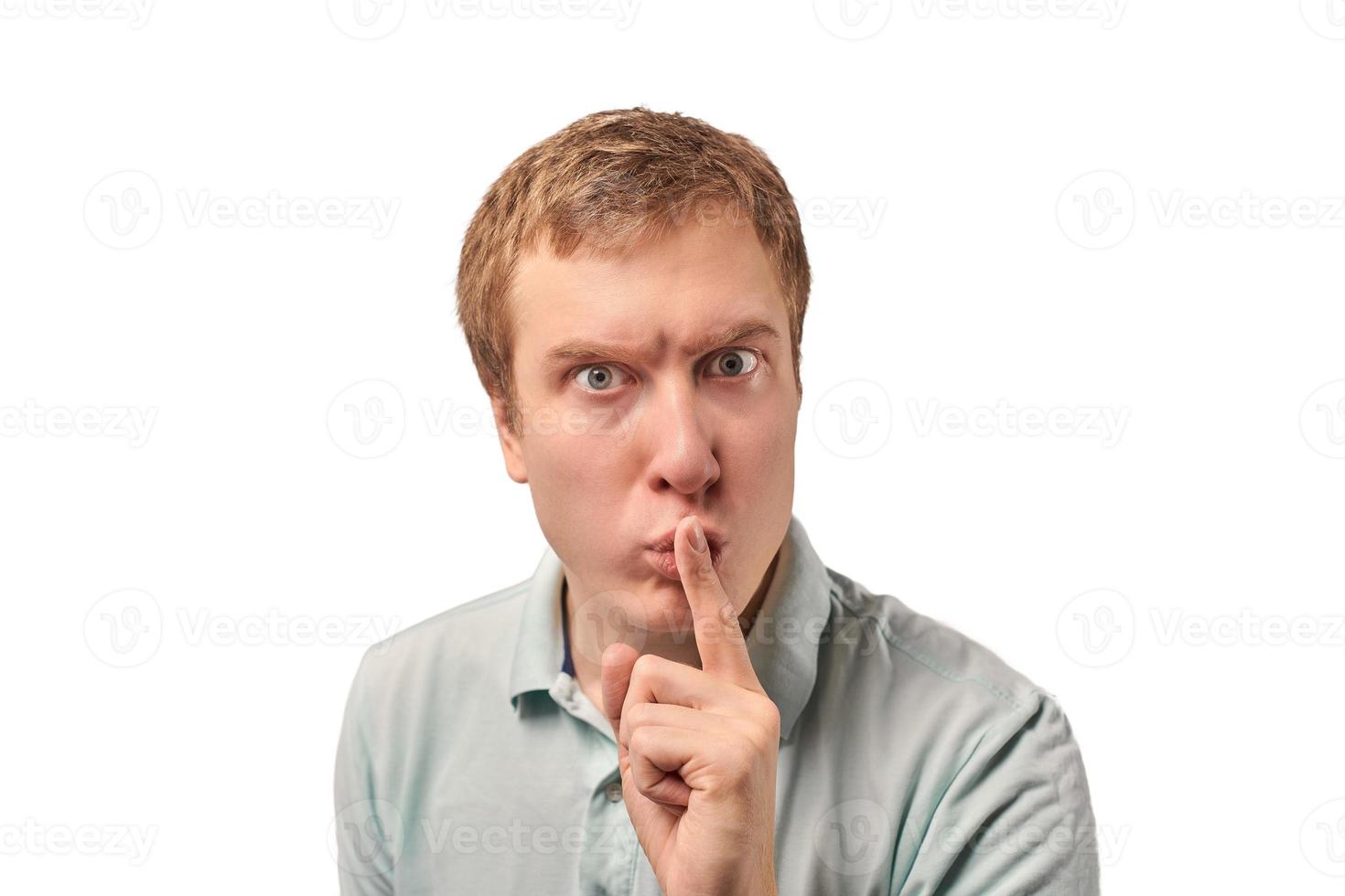 Funny guy in light gray Polo T-shirt asking to be quiet, silence gesture, white background photo