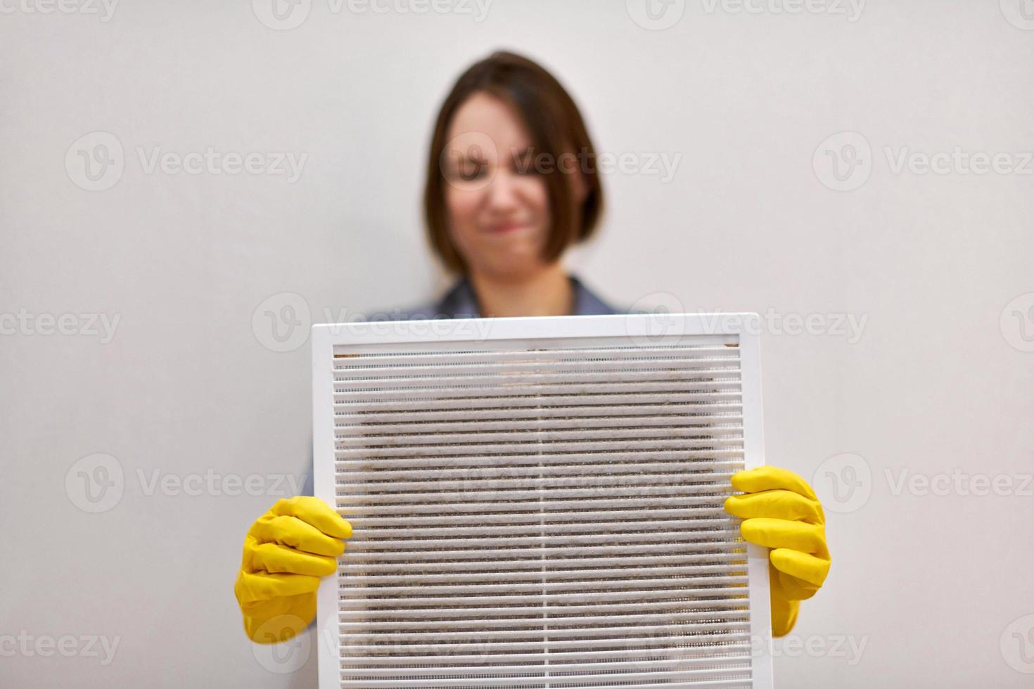 Woman holding dirty and dusty ventilation grille, disgusted photo