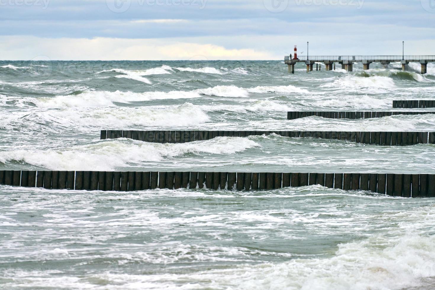 View of blue sea with foaming waves and wooden breakwaters photo