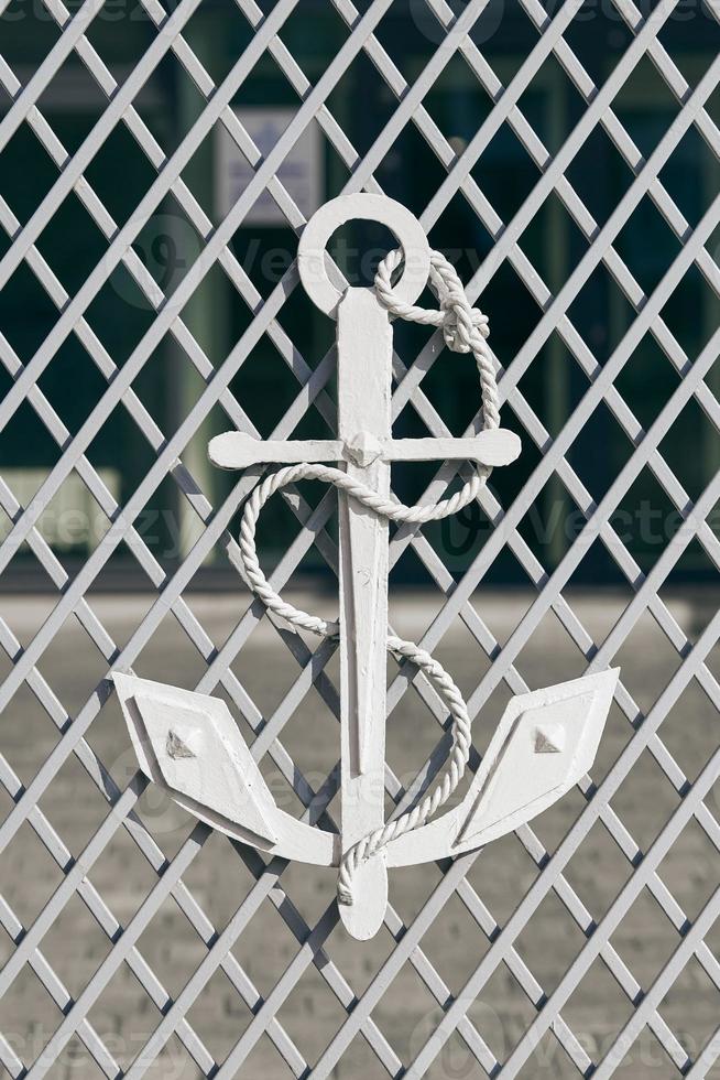 White anchor with mooring rope on mesh fence as symbol of navigation and maritime photo