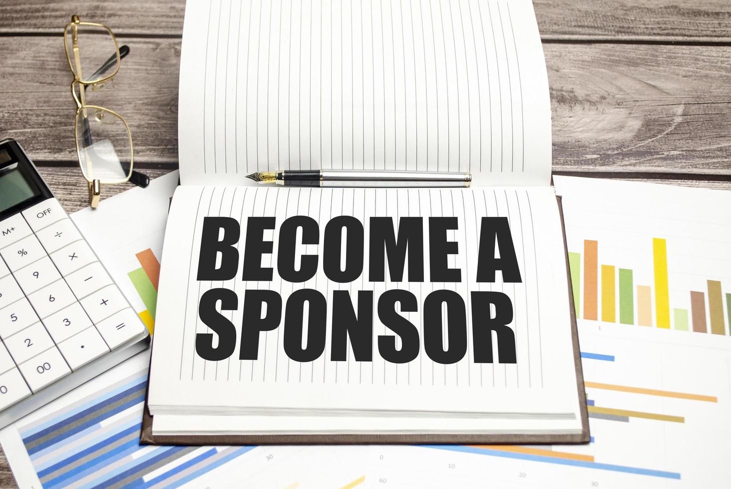 BECOME A SPONSOR on notepad and charts with calculator photo