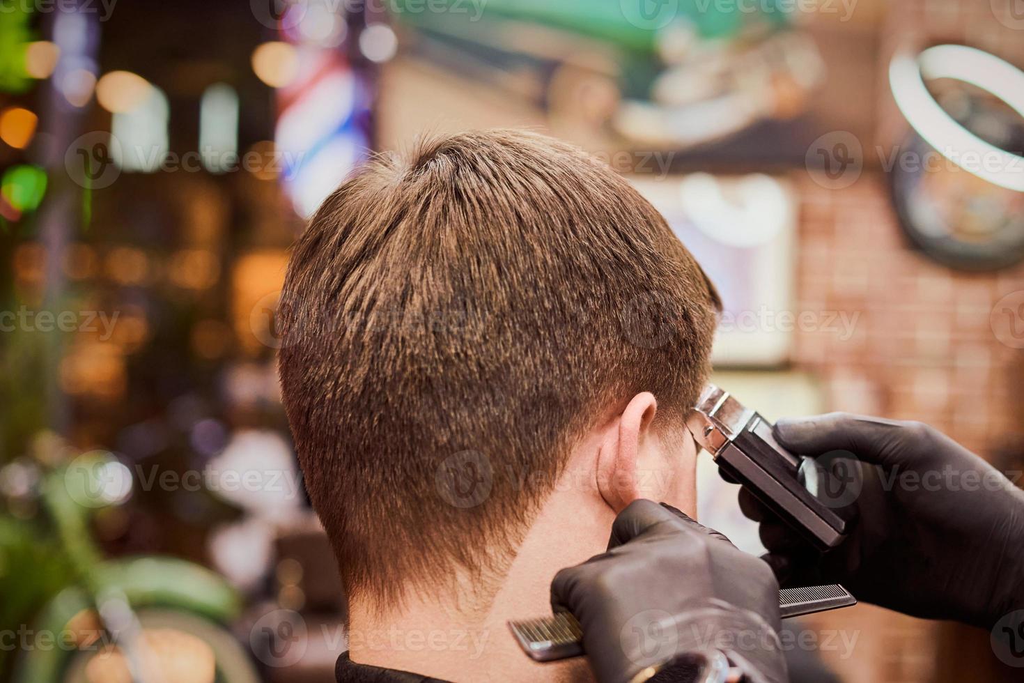 Male haircut shaving in barbershop, client getting haircut by hairdresser with electric shaver photo