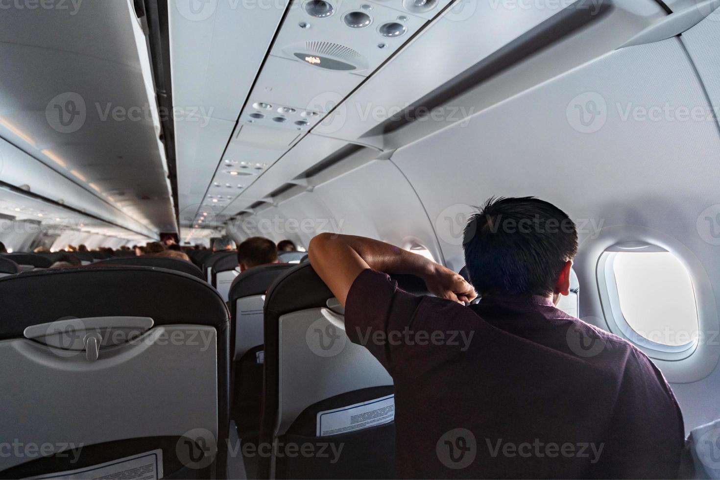 Man looks in airplane window. New aircraft cabin with comfortable seats. Economy class flight of new airline without flight delay. photo