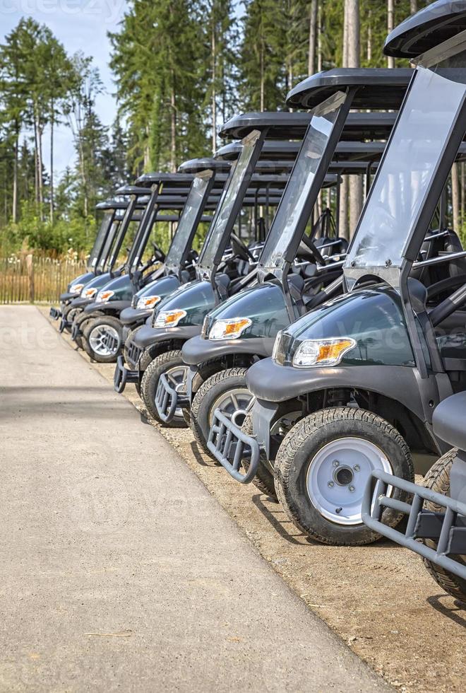 Golf cars or golf carts parked in a row outdoors on a sunny day. Vertical view photo