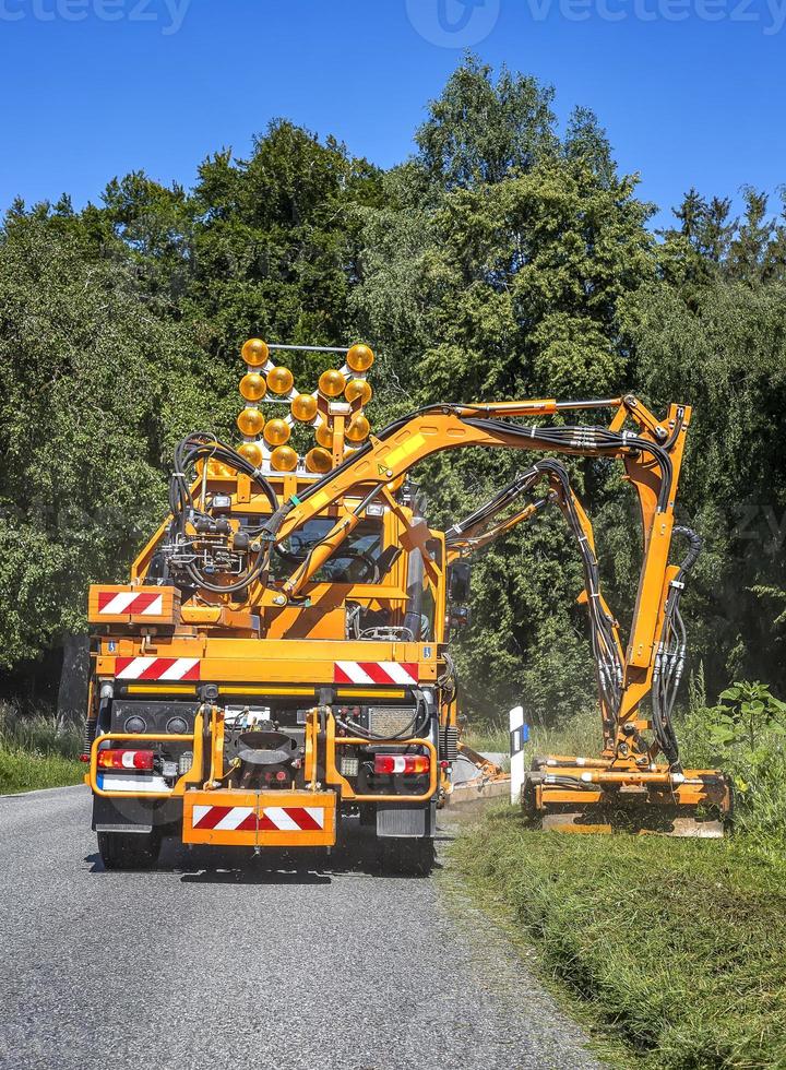 Tractor with a mechanical mower mowing grass on the side of the asphalt road. Road services are engaged in landscaping around roads. Vertical view photo