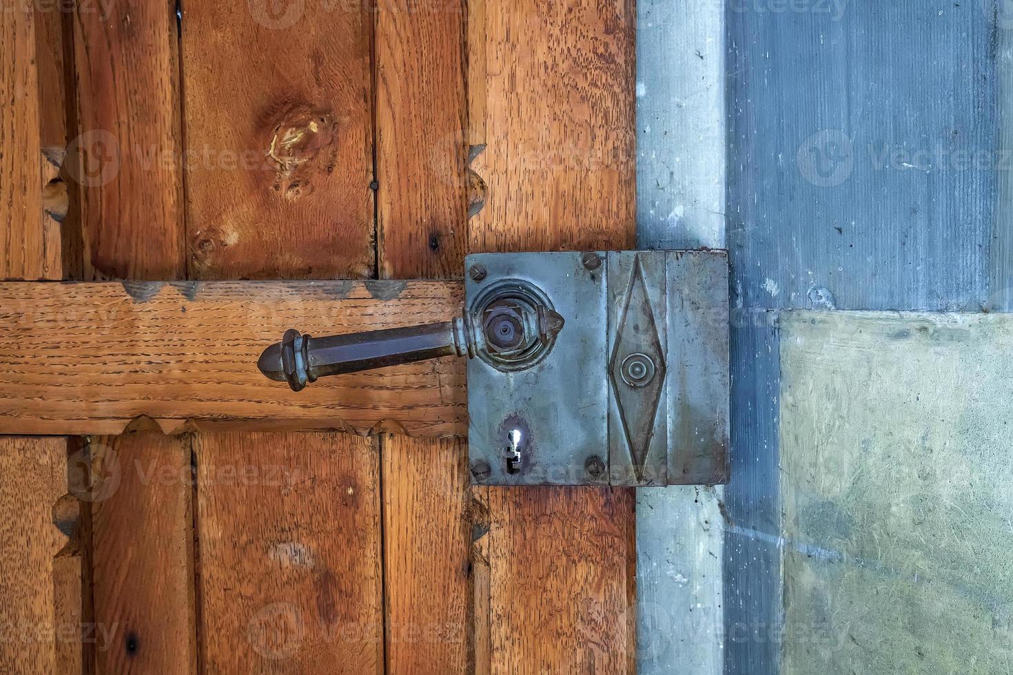 Fragment of an old wooden door with a forged steel handle. photo