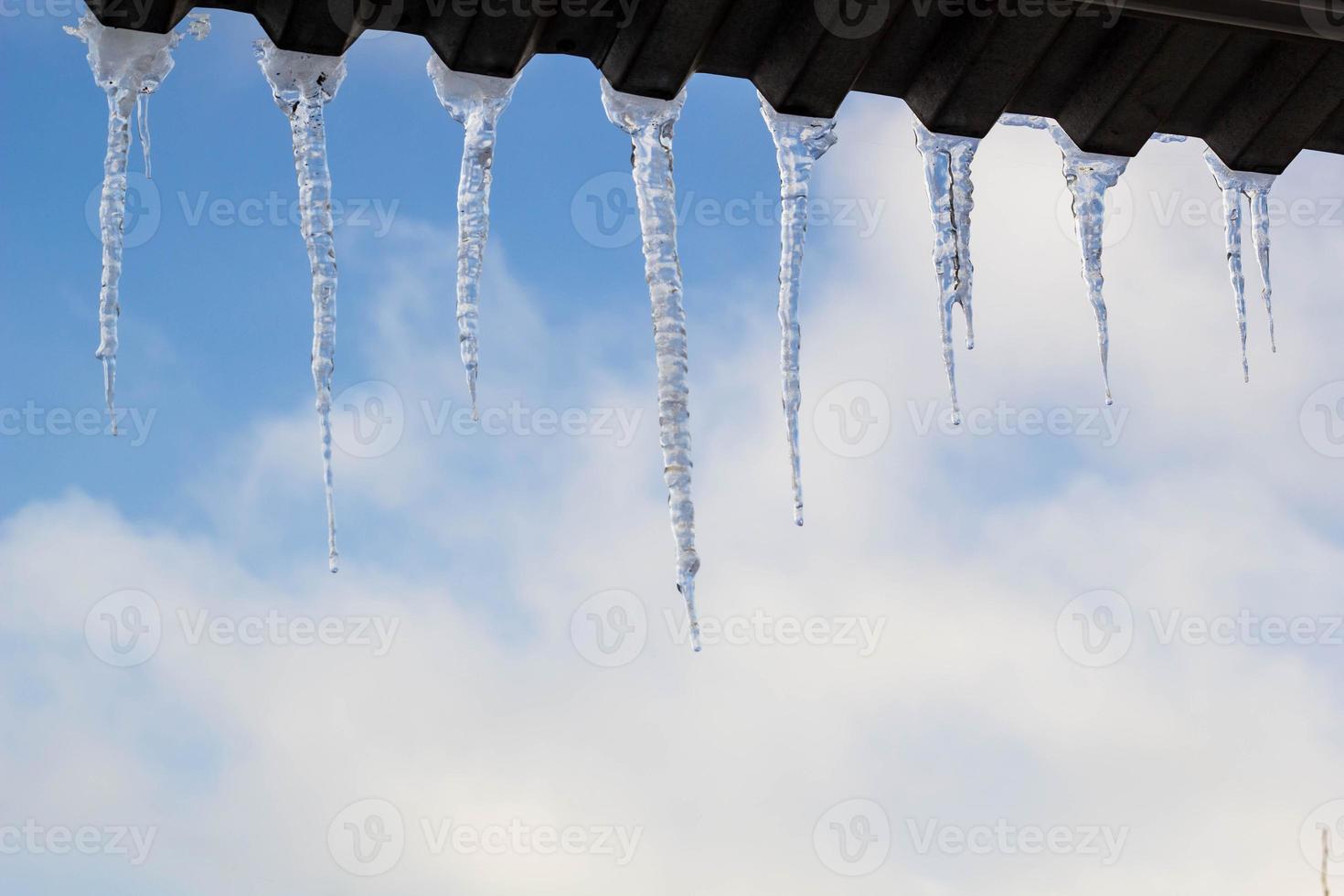 carámbanos colgando del techo en invierno. formación de hielo natural de cristales de hielo colgando en el borde del techo en invierno foto